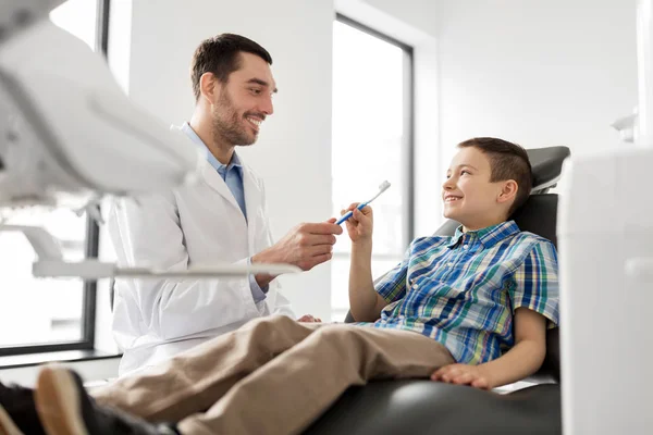 Стоматолог, дающий зубную щетку ребенку в клинике — стоковое фото