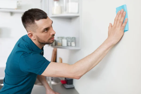 Muž s čistícím hadříkem na stěnu doma kuchyň — Stock fotografie