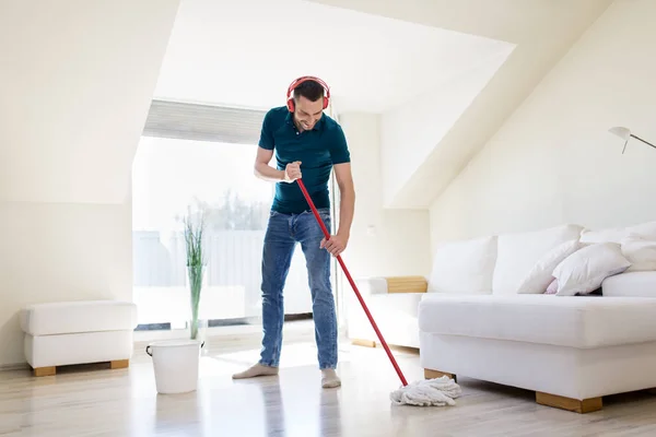 Hombre en auriculares limpieza piso por fregona en casa —  Fotos de Stock