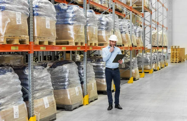 Geschäftsmann mit Helm und Klemmbrett in Lagerhalle — Stockfoto