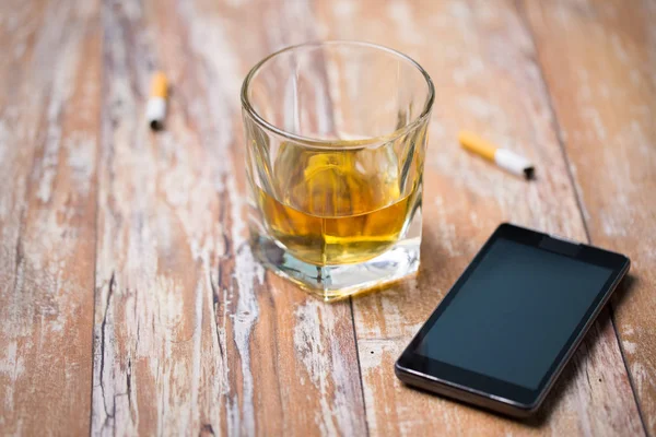 Glass of alcohol and smartphone on table — Stock Photo, Image