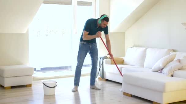 Чоловік в навушниках прибирає підлогу мопедом вдома — стокове відео