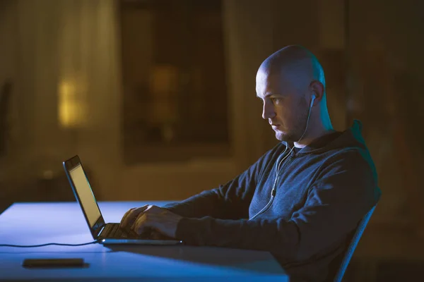 Hacker en los auriculares escribiendo en el ordenador portátil en la habitación oscura —  Fotos de Stock