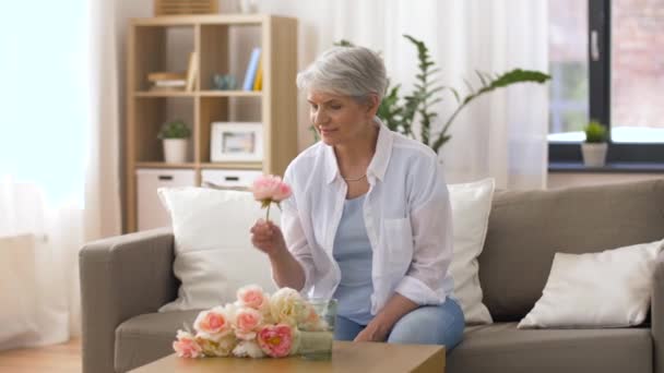 Lycklig senior kvinna att sätta blommor till vas hemma — Stockvideo