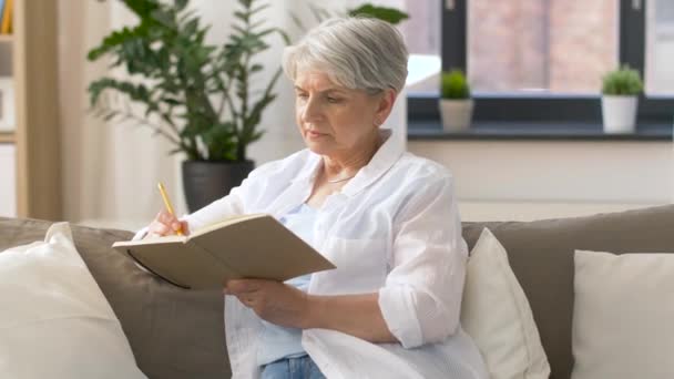 Senior vrouw schrijven naar notebook of dagboek thuis — Stockvideo