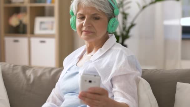人和生活方式概念 愉快的资深妇女在耳机和智能手机在家里听音乐 — 图库视频影像