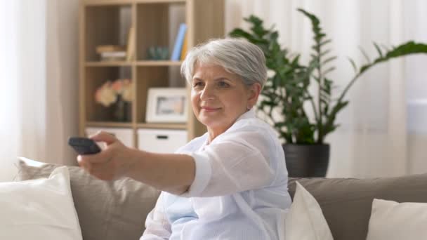 Mujer mayor con control remoto viendo la televisión en casa — Vídeos de Stock