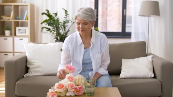 Щаслива старша жінка кладе квіти до вази вдома — стокове відео