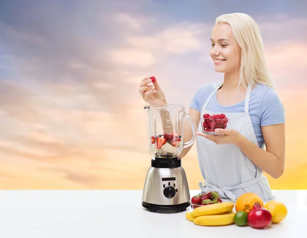 Mulher sorridente adicionando frutas e bagas ao liquidificador — Fotografia de Stock