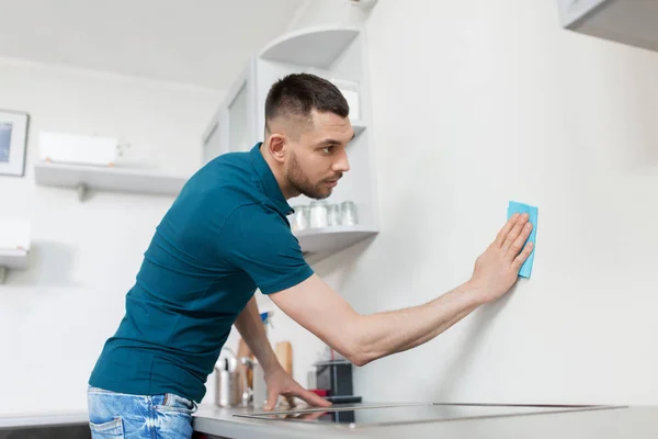 Muž s čistícím hadříkem na stěnu doma kuchyň — Stock fotografie