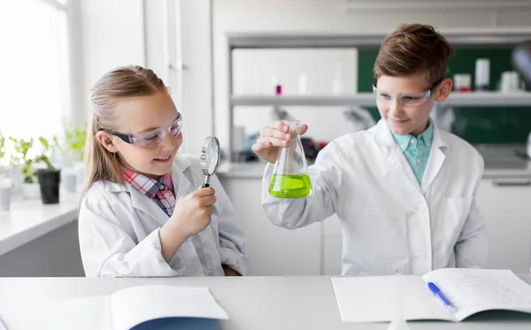 Дети с фляжкой и увеличителем на уроке химии — стоковое фото