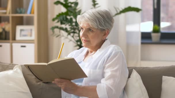 Írás jegyzetfüzet vagy napló otthon idősebb nő — Stock videók