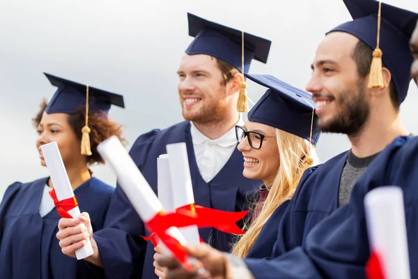 Happy students in mortar boards with diplomas — Stock Photo, Image