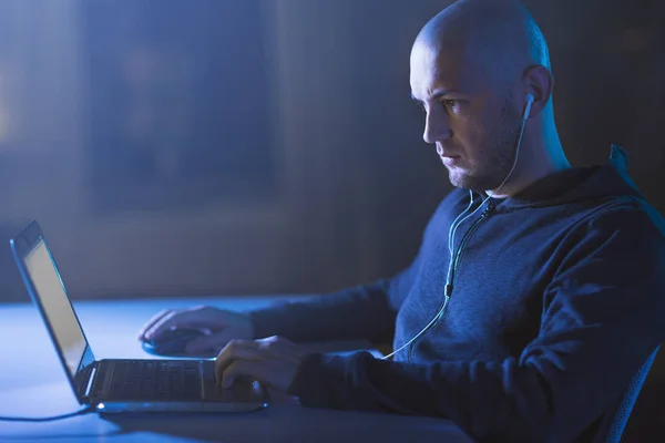 Hacker em fones de ouvido digitando no laptop no quarto escuro — Fotografia de Stock