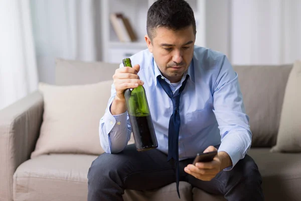 Homem com smartphone e garrafa de álcool em casa — Fotografia de Stock