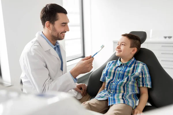 Dentista con cepillo de dientes y niño paciente en la clínica —  Fotos de Stock