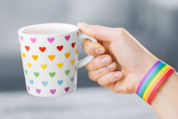 hand with cup of cacao and gay awareness wristband