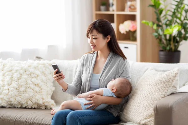 Mother with sleeping baby and smartphone at home — Stock Photo, Image