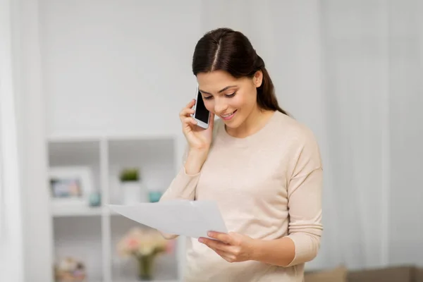 Vrouw met papieren bellen op smartphone thuis — Stockfoto
