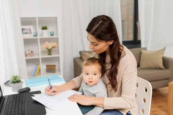 Glückliche Mutter mit Baby und Papieren, die zu Hause arbeiten — Stockfoto