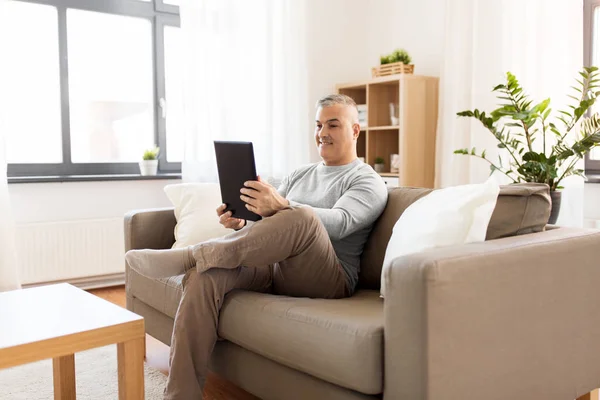 Hombre con tablet pc sentado en el sofá en casa — Foto de Stock
