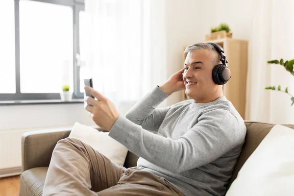 Homem com smartphone e fones de ouvido em casa — Fotografia de Stock