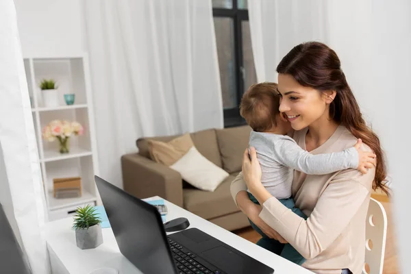 Mãe feliz com bebê e laptop trabalhando em casa Fotografias De Stock Royalty-Free