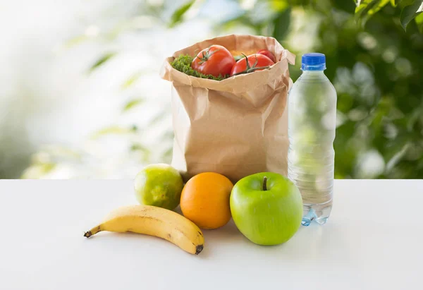 Бумажный пакет с овощной пищей и водой на столе — стоковое фото