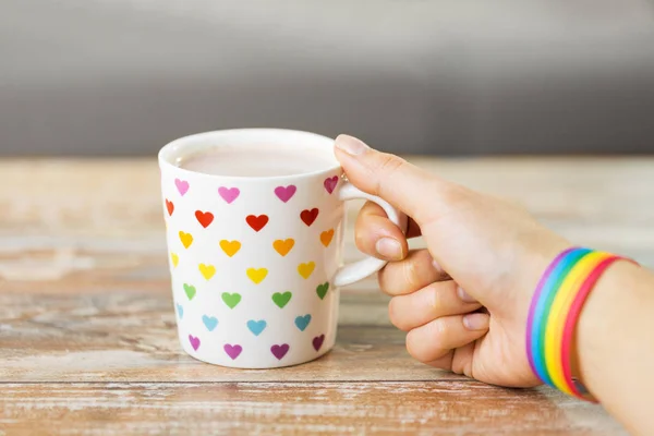 hand with cup of cacao and gay awareness wristband