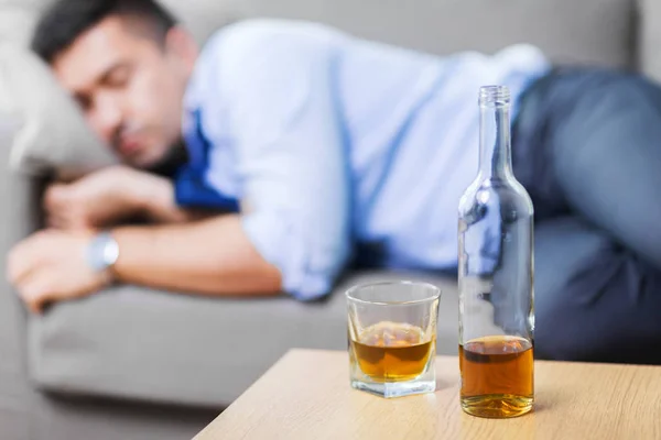 Bottle of alcohol on table and sleeping drunk man — Stock Photo, Image