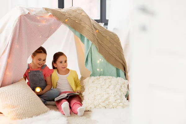 Girls with book and torch in kids tent at home — Stock Photo, Image