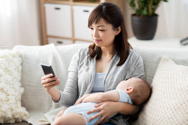 Mère avec bébé endormi et smartphone à la maison — Photo