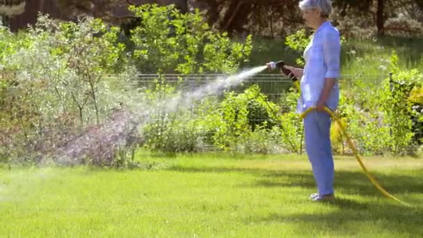 Пожилая женщина поливает газон из шланга в саду — стоковое видео