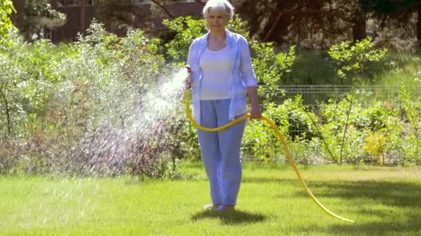 Senior vrouw gazon water door de slang op de tuin — Stockvideo