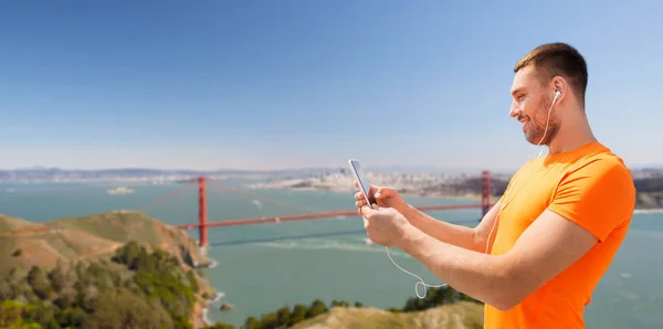 Man with smartphone and earphones over golden gate — Stock Photo, Image