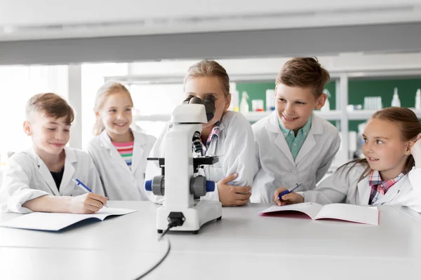 Niños o estudiantes con biología de microscopio en la escuela — Foto de Stock