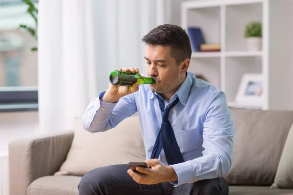 Алкоголик со смартфоном, пьющий пиво дома — стоковое фото