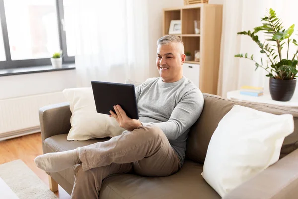 Uomo con tablet pc seduto sul divano di casa — Foto Stock