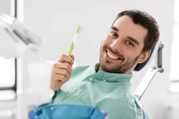 Uomo sorridente con spazzolino da denti alla clinica dentale — Foto Stock