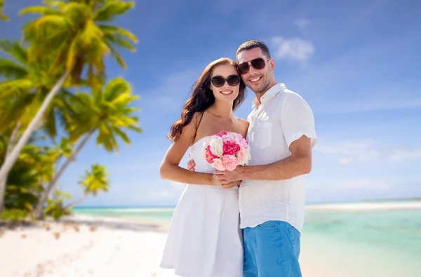 Happy couple with flowers over tropical beach — Stock Photo, Image