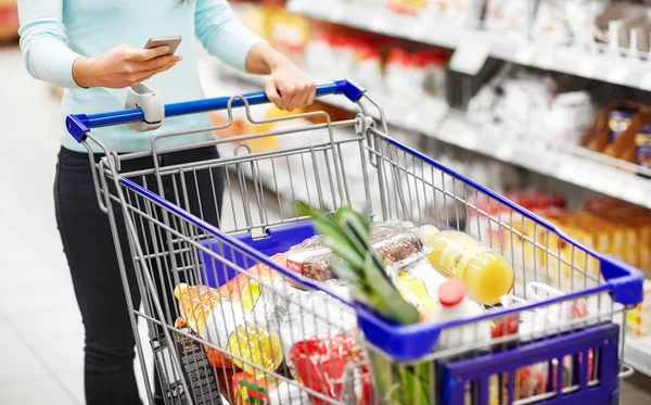 Vrouw met smartphone kopen van eten in supermarkt — Stockfoto