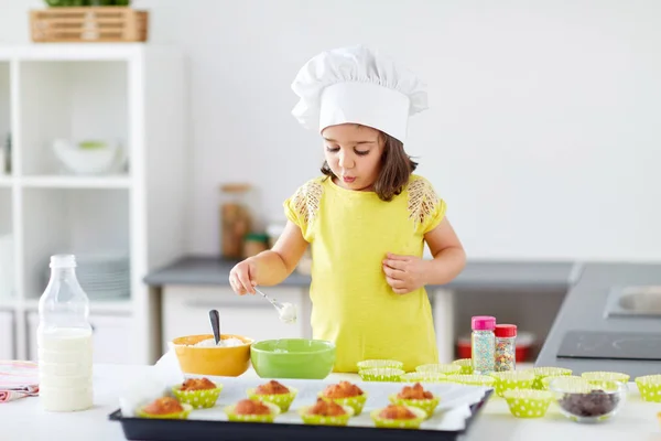 Liten flicka i kockar toque Baka muffins hemma — Stockfoto