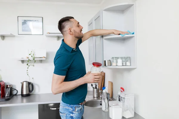 Homme avec chiffon nettoyage armoire de cuisine à la maison — Photo