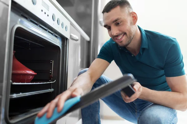Mannen med trasa för rengöring ugnsluckan på hem kök — Stockfoto