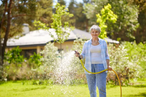 Пожилая женщина поливает газон из шланга в саду — стоковое фото