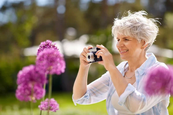 Mulher sênior com câmera fotografar flores — Fotografia de Stock