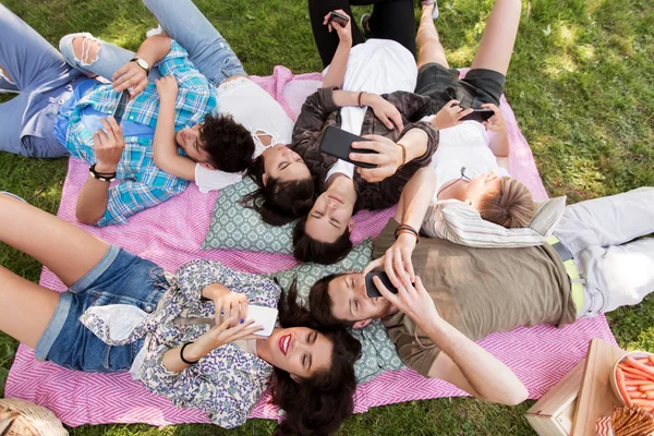 Amigos con teléfonos inteligentes en manta de picnic — Foto de Stock