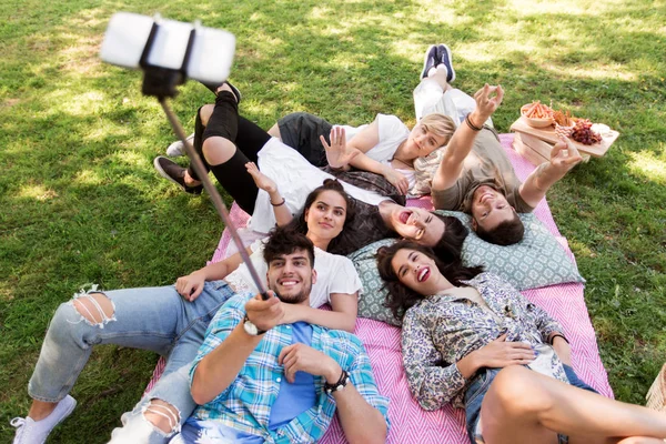 Friends taking picture by selfie stick at picnic — Stock Photo, Image