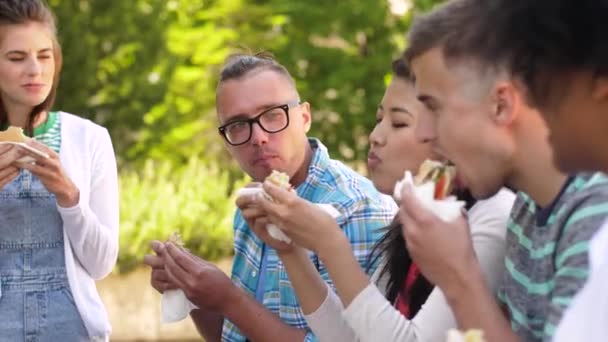 Amigos comiendo sándwiches o hamburguesas en el parque — Vídeo de stock