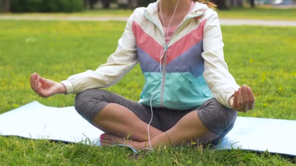 Mulher com fones de ouvido meditando no parque — Vídeo de Stock